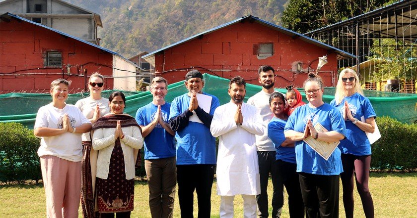 International yoga students and teachers standing together in namaste pose during yoga teacher training in Rishikesh, India.