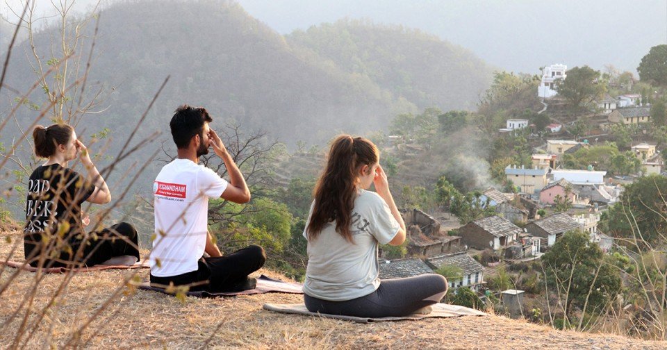 Yoga students practicing breathing meditation outdoors overlooking the hills of Rishikesh, India.